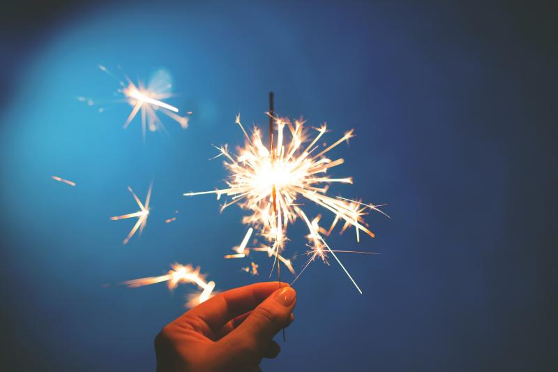 A sparkler held up the night sky. Tight cropped to just the fingers and sparks