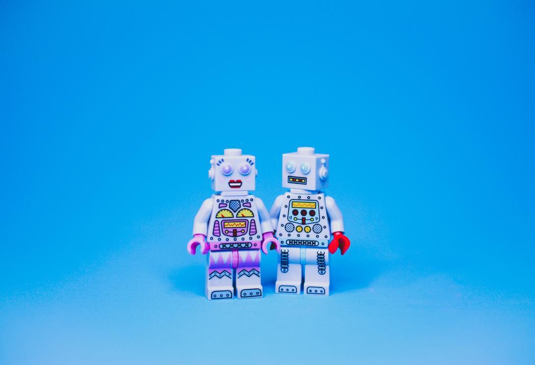 Two robot legos standing close to each other on a blue background